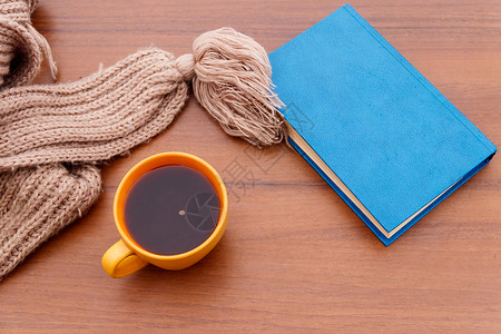 一杯咖啡针织围巾和木制背景的书图片