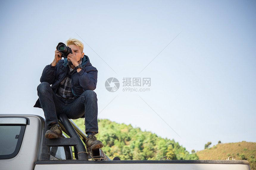 年轻摄影师坐在小卡车上拍摄山上照片图片