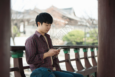 年轻男子在韩国传统房屋中背包旅行请使用您的智能手机Smart图片