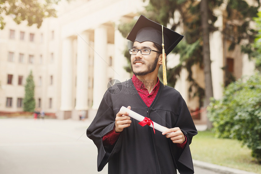 年轻微笑的男在毕业日获得大学文凭图片