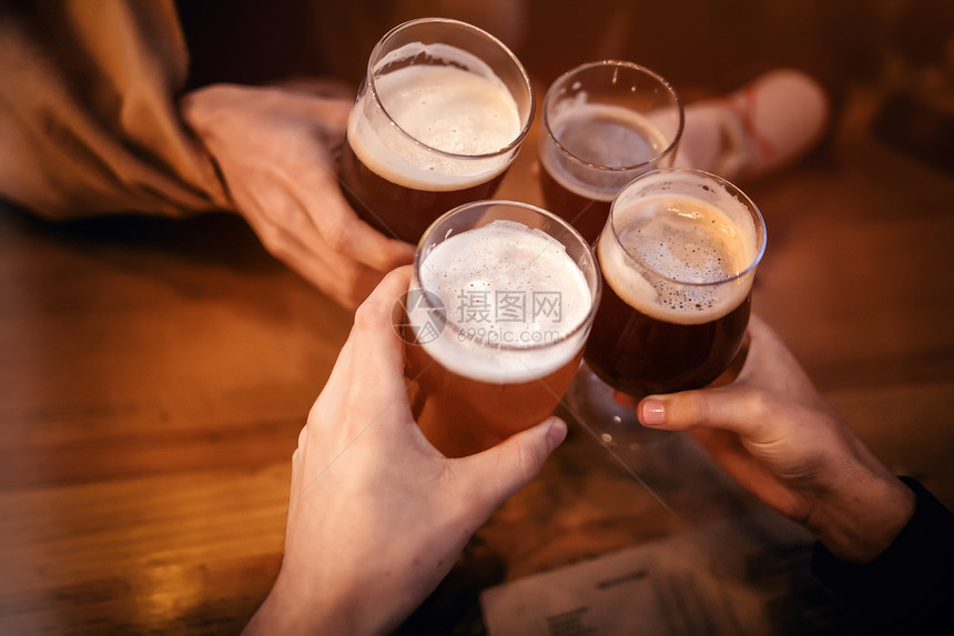朋友们在酒吧里用美味的精酿啤酒碰杯和敬酒一群人在酒吧欢呼和享受啤酒手里拿着杯啤酒休图片