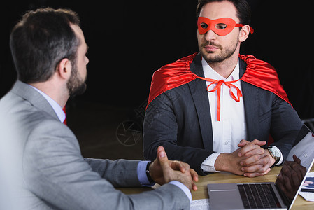 戴着面具和披斗篷的超级商人与办公室中的商人交谈时被图片