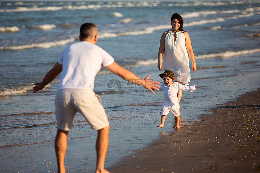 年轻快乐的家庭在白天沿着海边散步爸在前面等着他的儿子小男孩从妈跑到爸图片
