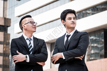 两名身穿黑西装的亚洲青年商人与办公大楼背景站图片