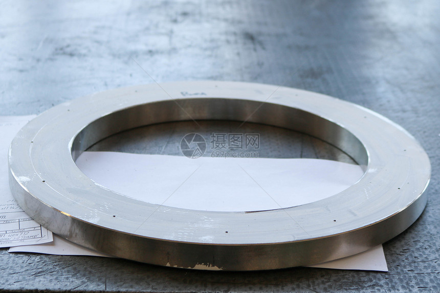 工厂车间的工作铁桌上有一个带小孔法兰的大圆形闪亮金属环制图片