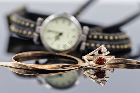 优雅的金戒指和链条位于带皮革表带的女士手表的背景上图片