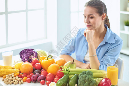坐在厨房里的快乐的年轻家庭主妇准备食物从一堆不同的新鲜有机水果和蔬菜图片