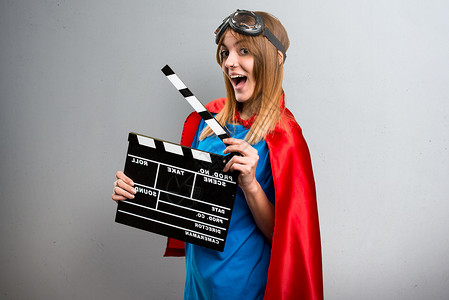 漂亮的超级英雄女孩拿着一个锁板在灰背景图片