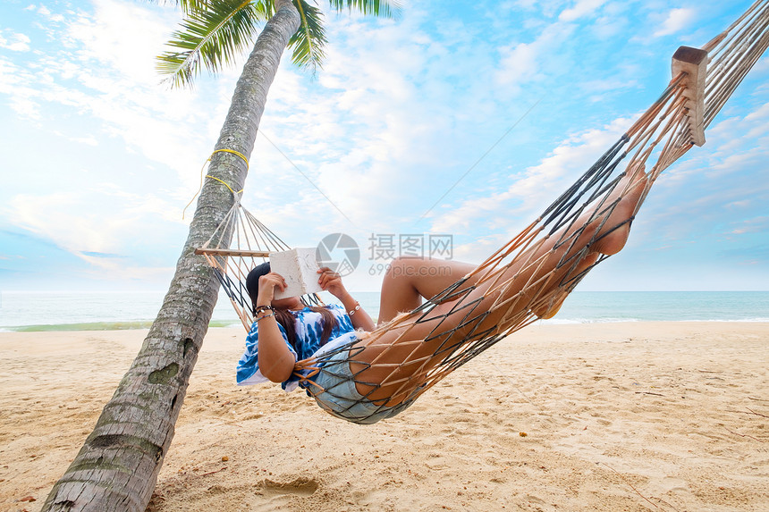 夏季休闲感女美丽晒黑在热带沙滩的吊床上享受日光浴放松和阅读书籍图片