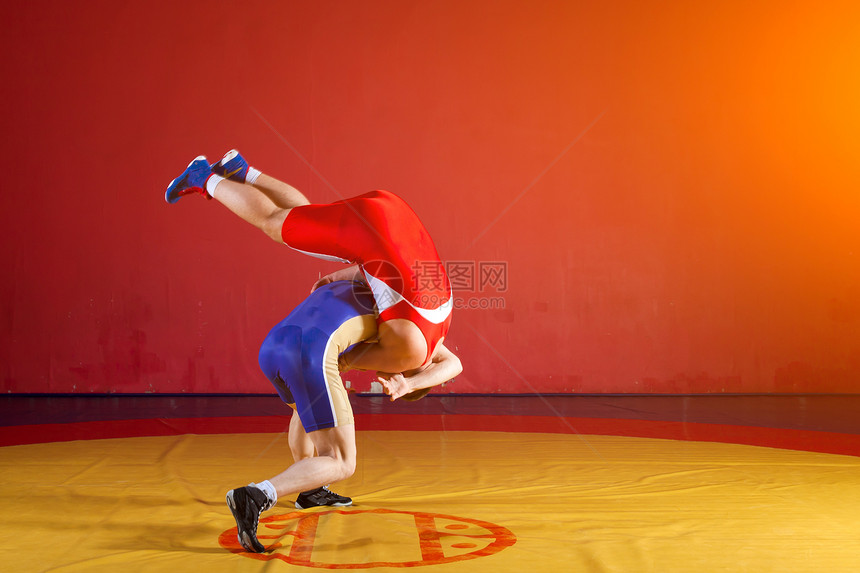 在健身房的黄摔跤地毯上穿着红制服和蓝制服摔跤的两位希腊图片