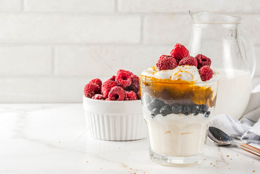 健康的早餐以牛奶油焦糖和浆果白大理石桌复制空间装在玻璃中的塞图片
