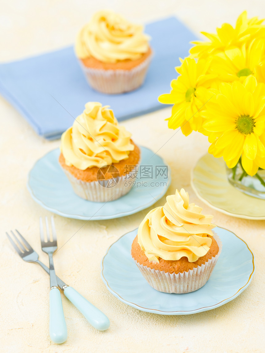 黄色奶油色装饰的纸杯蛋糕和黄色柔和背景玻璃中的黄色菊花束图片