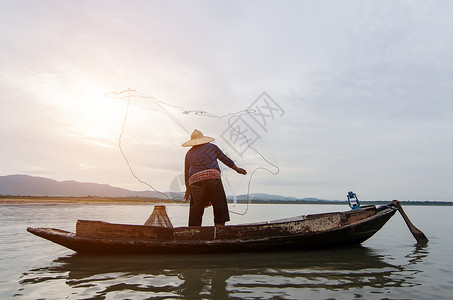 亚洲渔民在日出前的清晨在自然河中撒网捕淡水鱼的木船上图片