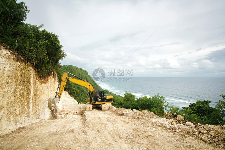 挖掘机在通往大海的岩石悬崖上工作景观与森林和海洋为建筑而砍图片
