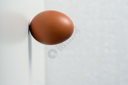 极简主义一个生鸡蛋水平站在白色背景的墙上勤奋耐力克服违图片