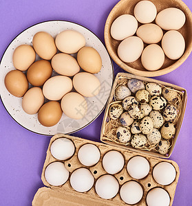 新鲜鹌鹑和鸡蛋装在木箱纸箱和紫色背景的盘子里图片