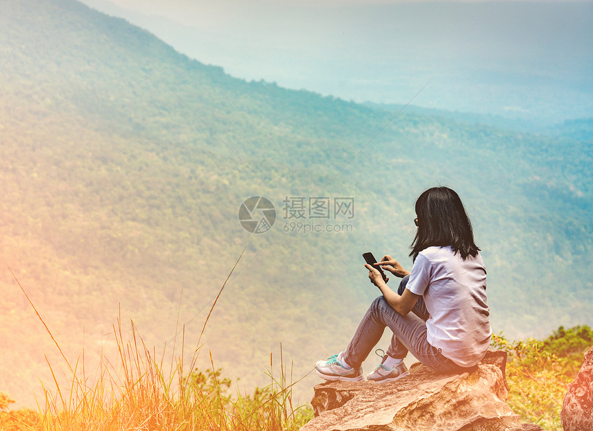年轻的亚洲女坐在悬崖边的岩石上图片