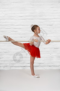 在健身房里穿着红色裙子的金发小芭蕾舞女演员微笑的肖像背景图片