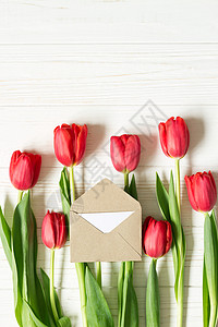 白色木制背景上的红色郁金香上的小信封风格平躺与复图片