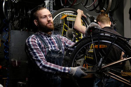 两个英俊的时尚男在修理店里用自行车工作工人在车间修理图片