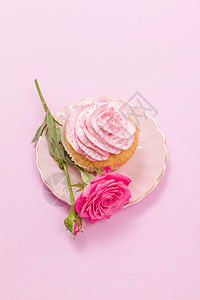 粉红色奶油装饰和粉红色柔和背景上的玫瑰的纸杯蛋糕图片