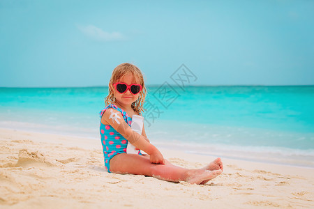 小女孩在海滩的肩膀上涂防晒霜图片