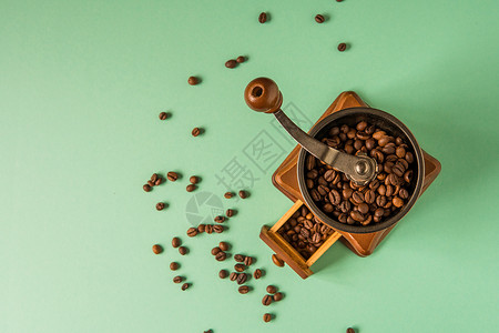 咖啡豆在手持咖啡研磨机中以绿色背景温图片