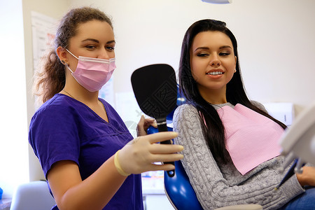 牙科女牙医在牙科柜里用镜子向病人展示新牙齿图片