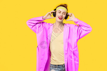 黄色背景的年轻女子和粉红色大衣拥抱着音乐蠕虫无线耳机彩色迷恋概念图片