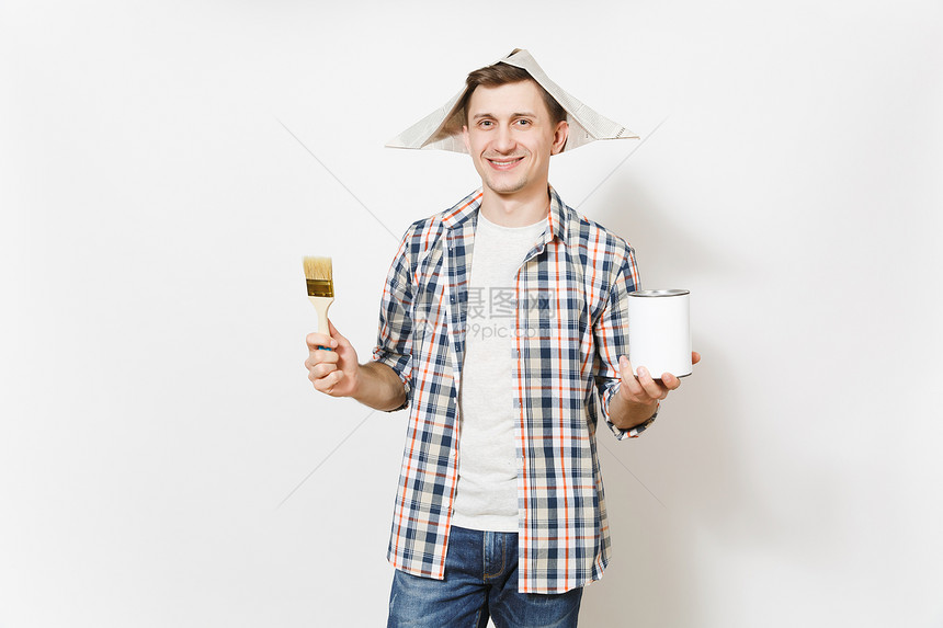 年轻微笑英俊的男人在报纸帽子拿着油漆刷和空油漆锡罐与副本空间隔离在白色背景图片