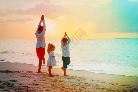 父亲带着儿子和女儿在日落热带海滩做瑜伽图片