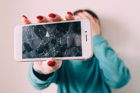 碎玻璃屏幕智能手机手在心烦意乱的女孩图片