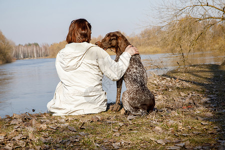 女人和狗坐在河岸上友谊的概念图片