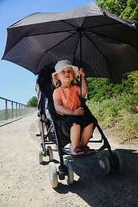坐在婴儿车里的小女孩用大伞保护孩子免受阳光照射夏季阳光明媚的日子图片