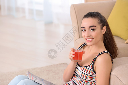 美丽的年轻女子在家读杂志时喝着柑图片