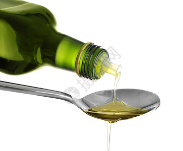 在白色背景上将橄榄油从瓶子里倒入勺子图片