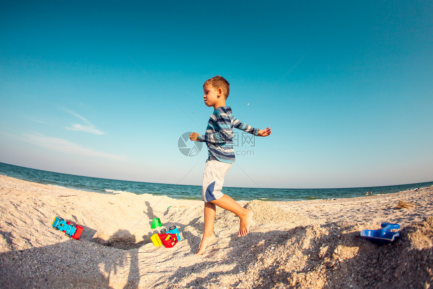 一个男孩正在沙滩上玩沙子孩子沿着海岸逆着天空奔跑孩子在大自然中玩得很开心这个图片