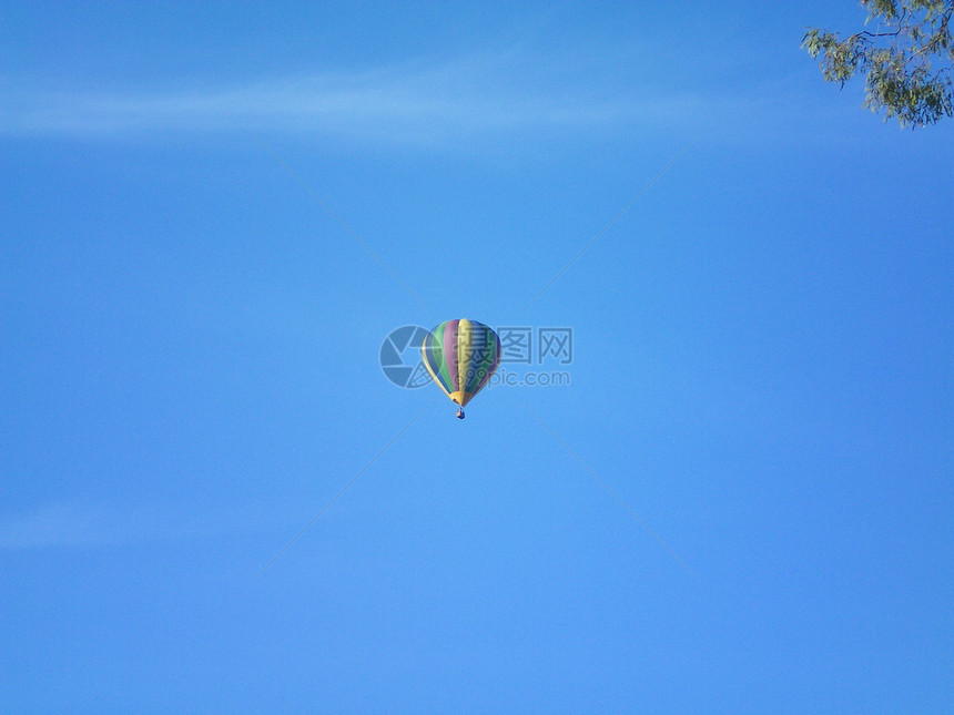 一个五颜六色的热气球漂浮在蓝天上有一些淡的白云气球的颜色是黄色绿色蓝色和紫色的条纹面板胶树的枝构成图片