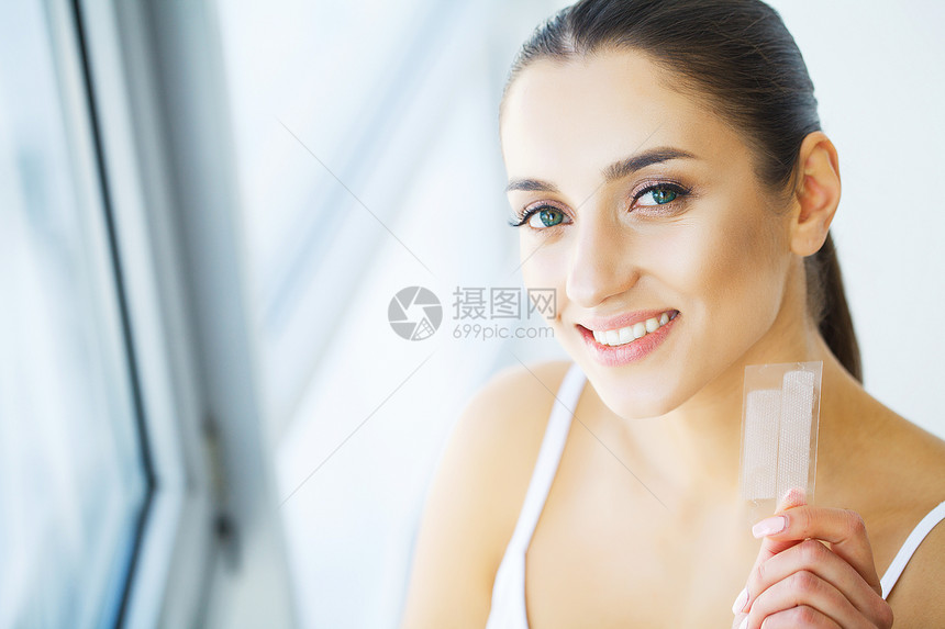 牙齿美白美丽的微笑的女人拿着美白带图片