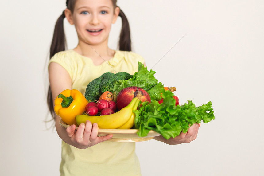 拿着盘子的逗人喜爱的小微笑的女孩画象用新鲜的蔬菜图片