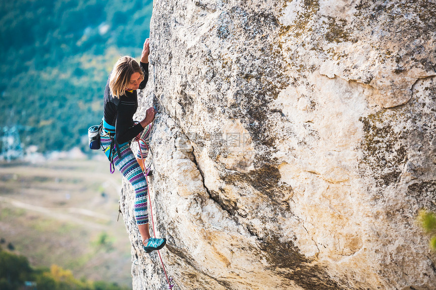 女孩爬上岩石登山者在自然浮雕上训练极限运动在大自然中进行积极的娱乐一位女士克服了艰图片