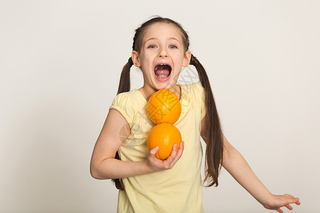 快乐的小女孩站在白色背景上用橘子玩得开心儿童健康食品概图片