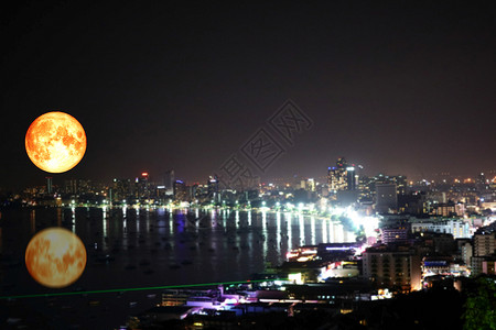 海上超级满血月反射和城市上空模糊夜光的色彩缤纷图片