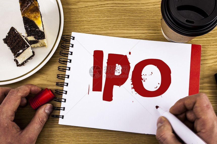 显示Ipo的概念手写展示首次公开募股的商业照片公司首次向公众开发行由ManNotebook木制背景蛋糕和杯图片