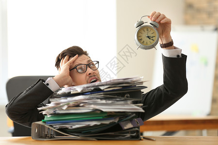 有闹钟和办公文件堆积在办公室的商人时图片