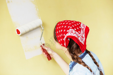 穿着红色头巾的漂亮女孩用油漆滚筒在墙上刷漆一位年轻美女在她的新公寓图片
