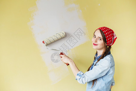 穿着头巾的漂亮女孩用油漆滚筒在墙上刷漆一位年轻美女在她的新公寓图片