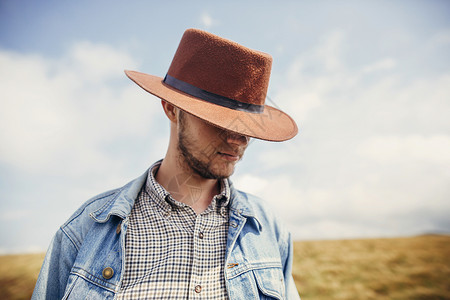 时尚旅行者留着胡子的男人戴着帽子站在阳光明媚的山顶上文本的空间时髦牛仔家伙肖像惊人的大气时刻背景图片