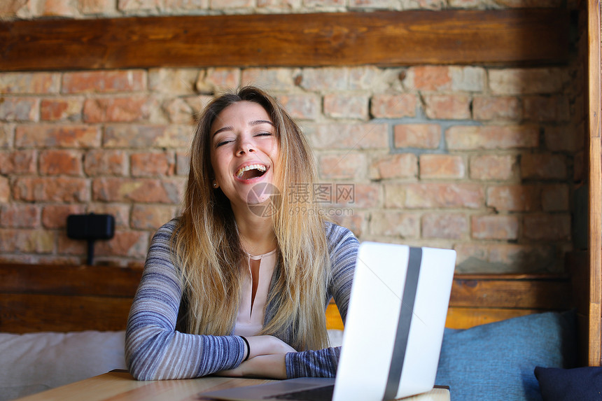在咖啡馆用笔记本电脑上网的笑女人快速互联网和自图片