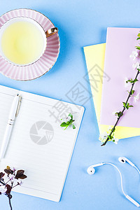 用耳机茶杯和蓝色背景的多彩笔记本打开笔记本配有花枝的图片